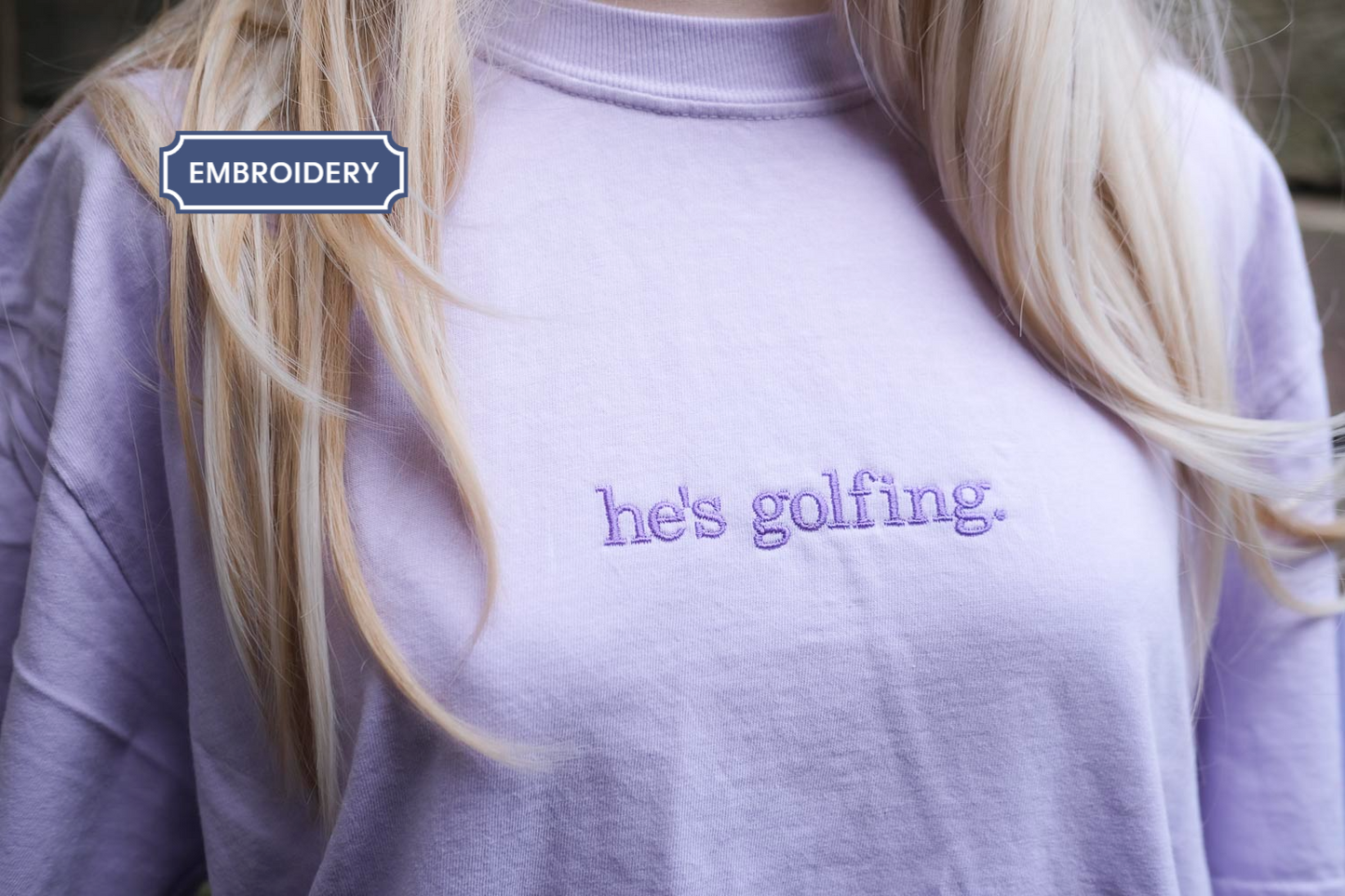 A person wearing a purple t-shirt with the text "he's golfing" printed on it.