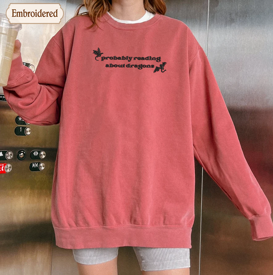 A person wearing a red sweatshirt with the text "probably reading about dragons" printed on it.