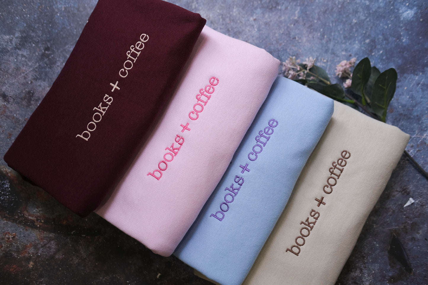 four books and coffee-themed shirts or tops, each with a different color and design, arranged in a row on a textured surface.
