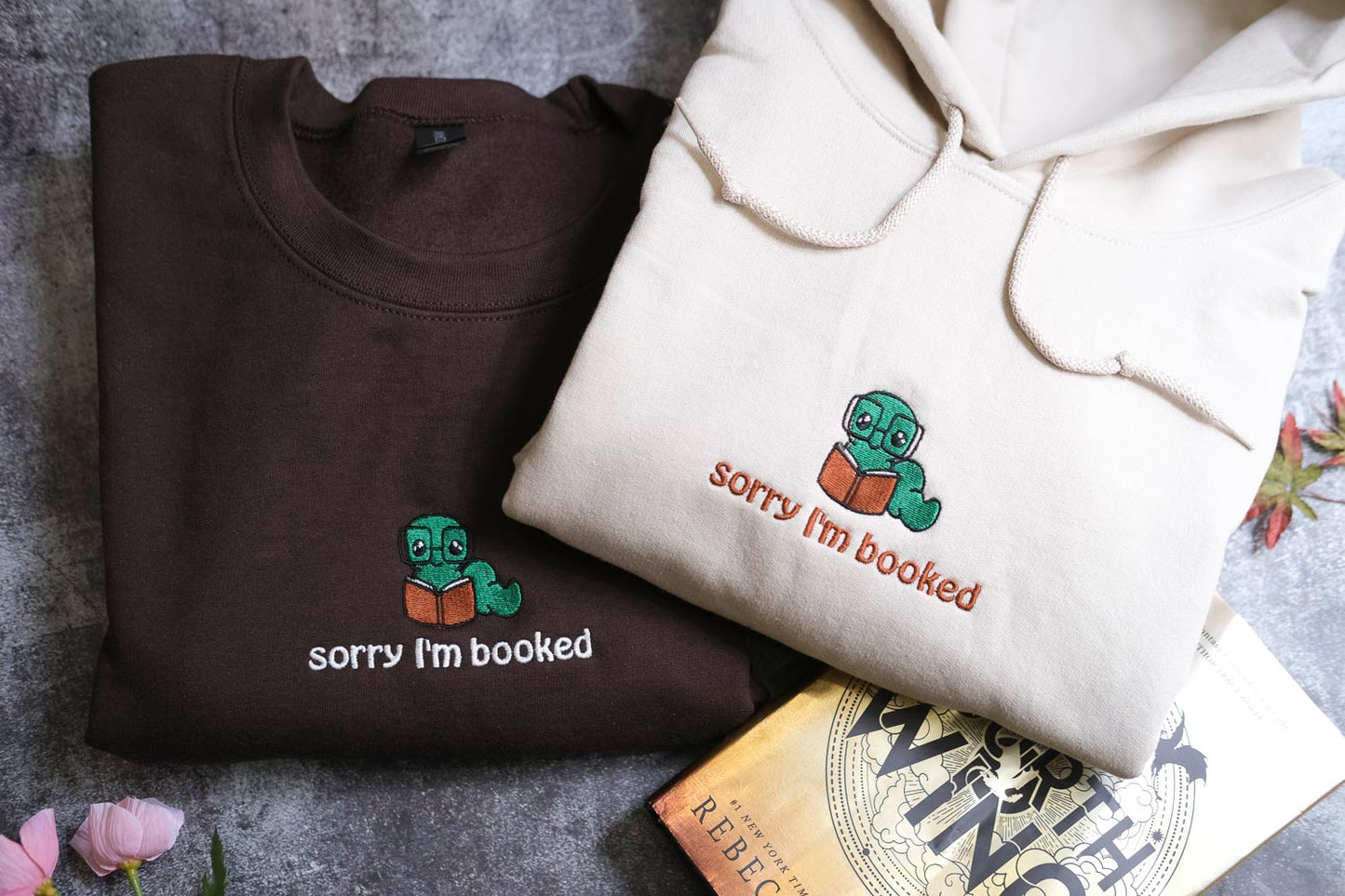 two t-shirts with a humorous text and a small green character on them, along with a book titled "The Wings of the Wisp".