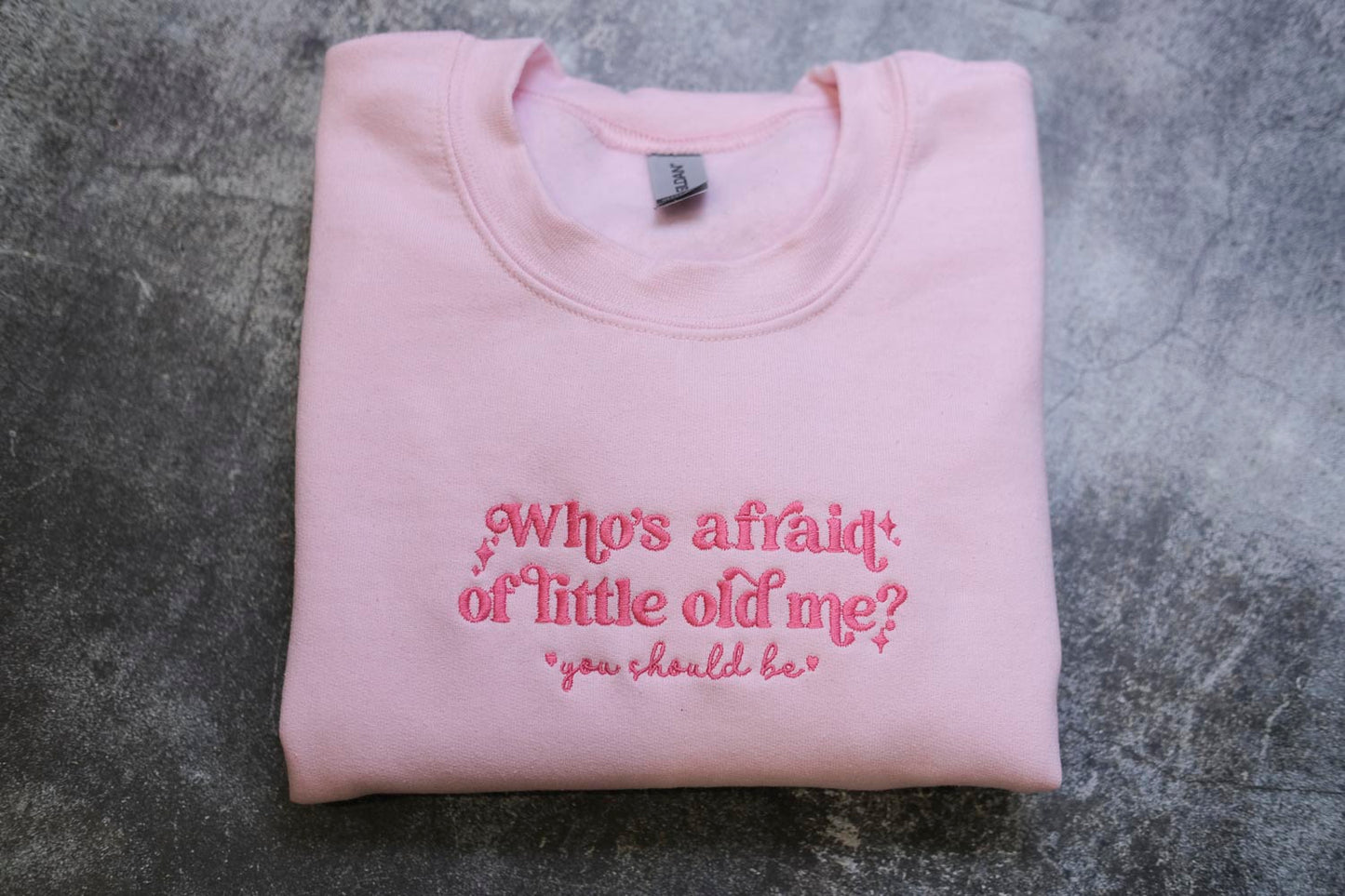 A pink sweatshirt with the text "Who's afraid of little old me? you should be" embroidered on it.