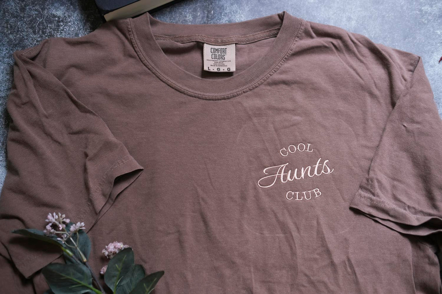 A brown t-shirt with the text "COOL AUNTS CLUB" printed on it, along with a small label on the collar.