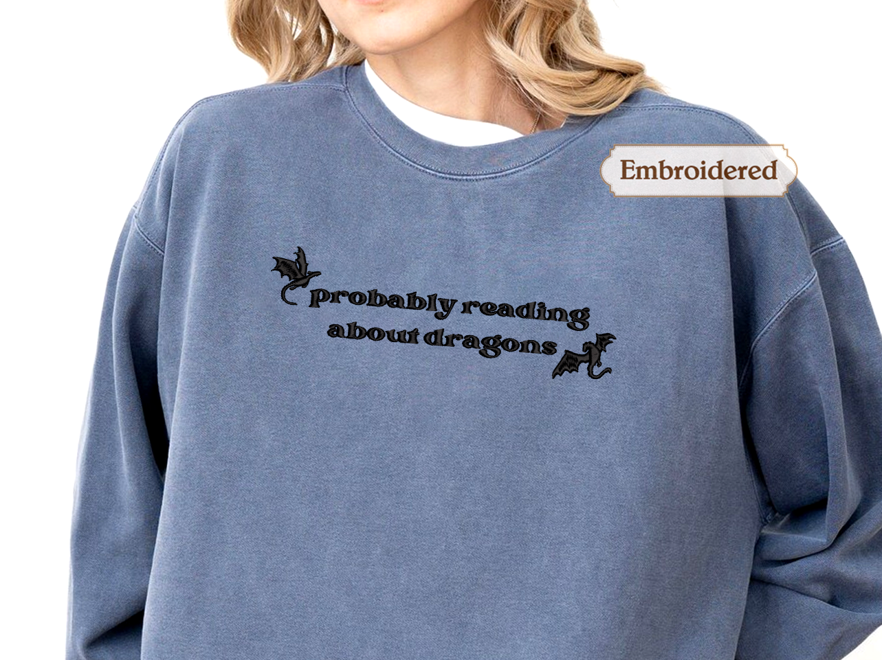 A person wearing a blue sweatshirt with the text "Probably reading about dragons" embroidered on it.