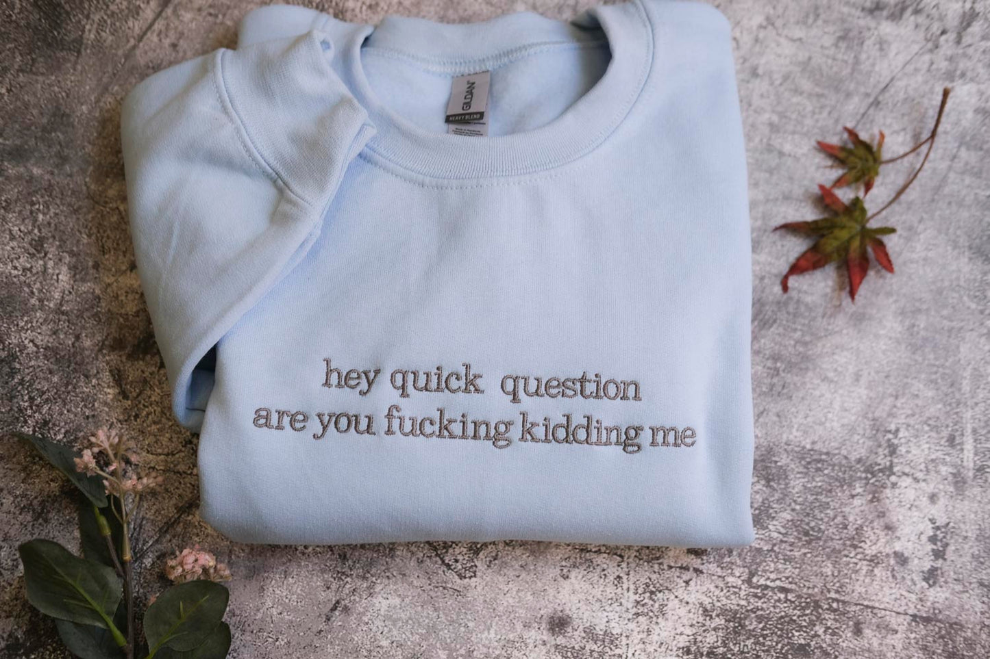 a light blue t-shirt with the text "hey quick question are you fucking Kiddin Me" printed on it, along with some leaves and flowers on the surface.