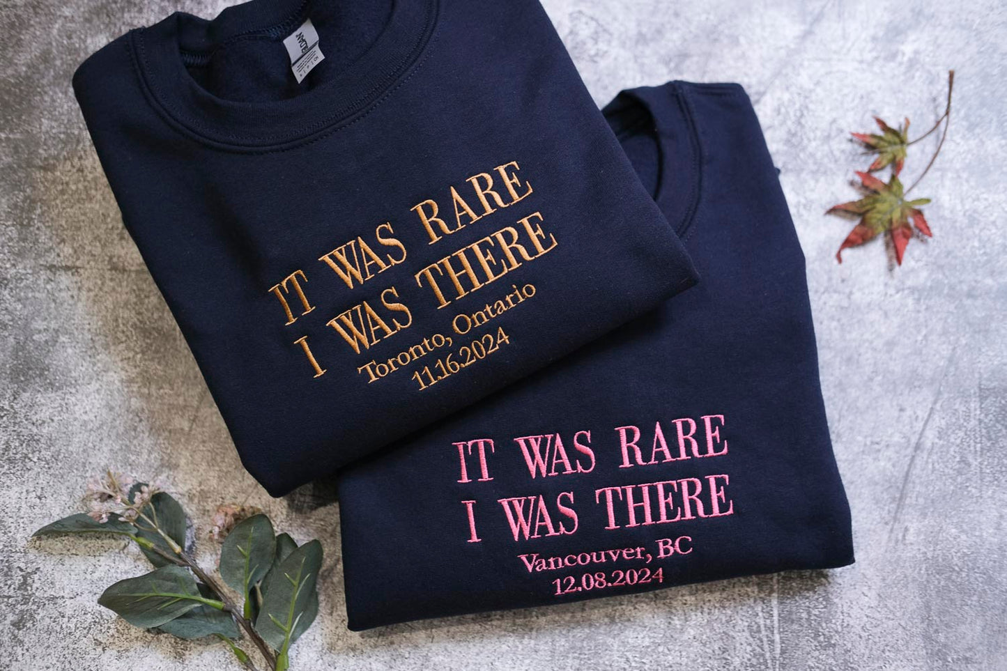 two navy blue sweatshirts with gold text, one reading "IT WAS RARE I WAS THERE" and the other reading "IT WAS RARE I WAS THERE Vancouver, BC".