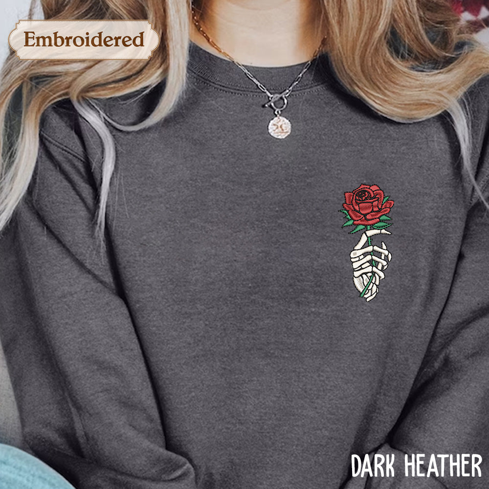 A person wearing a gray sweatshirt with a red rose embroidered on the front, along with a necklace and a pendant.