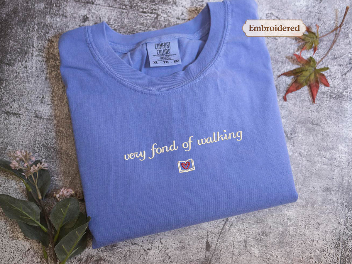 A blue t-shirt with the text "very fond of walking" printed on it, along with a small embroidered label and a leaf.