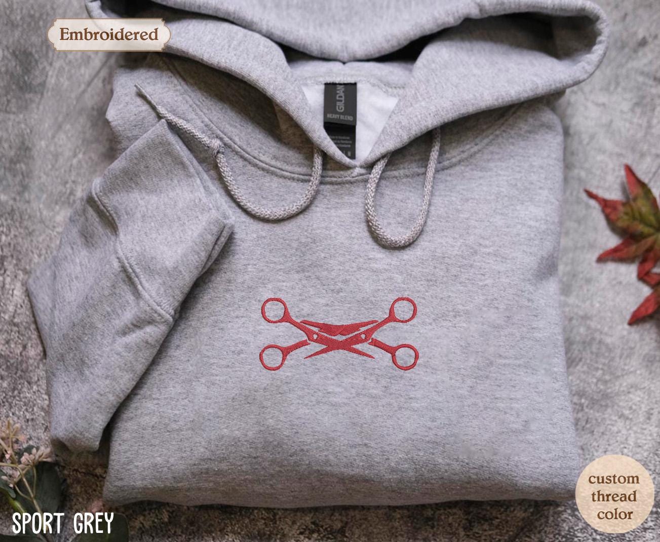a gray sweatshirt with a red scissors on it