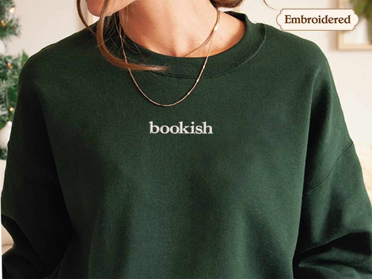 A person wearing a green sweater with the word "bookish" embroidered on it.