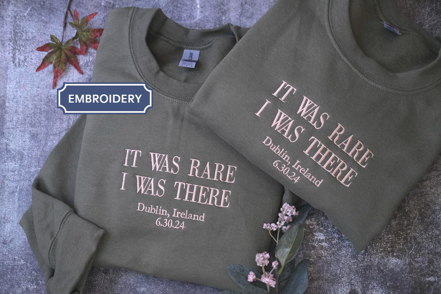 two gray sweatshirts with white text printed on them, placed on a gray surface.
