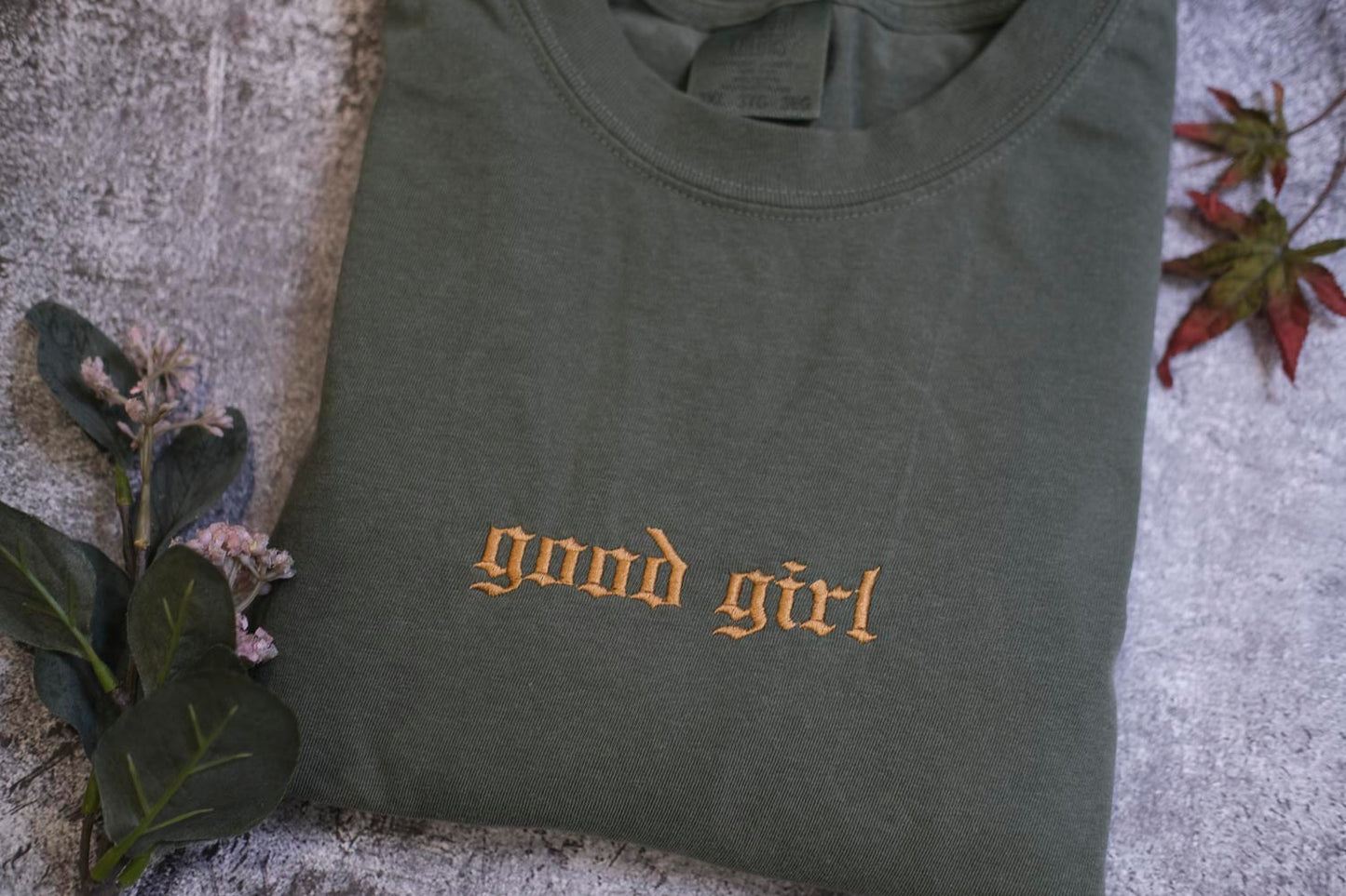 a gray t-shirt with the text "good girl" printed on it, along with some leaves and flowers.