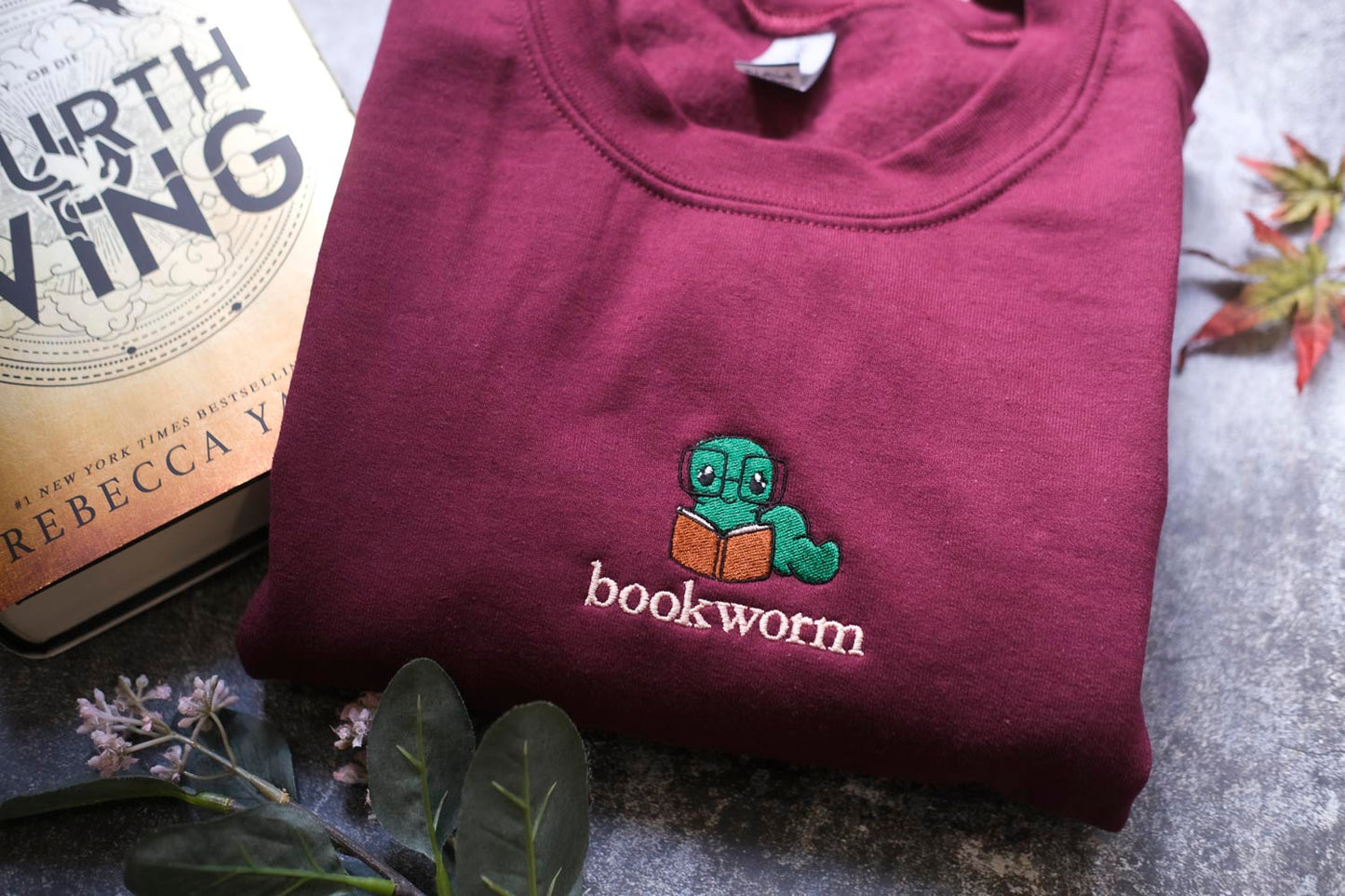 a maroon sweatshirt with a green book worm embroidered on it, along with a book titled "The Earthling" by Rebecca Yay.