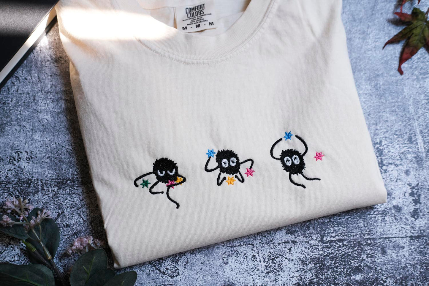a white t-shirt with three small black figures with colorful accents, each holding a star, arranged in a row.