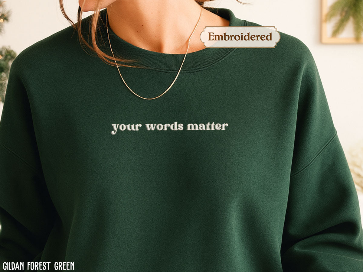 A close-up of a person wearing a green sweater with the text "your words matter" embroidered on it.