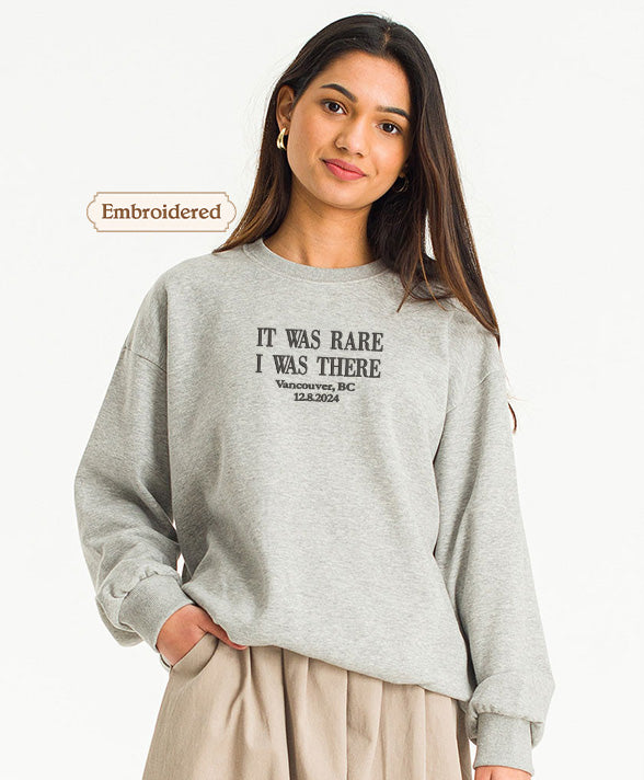 A young woman wearing a gray sweatshirt with the text "IT WAS RARE I WAS THERE VANCOUVER BC 14.04.20" printed on it.