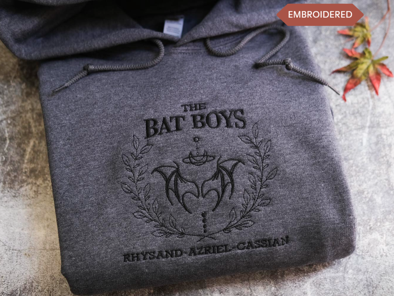 A gray hoodie with the text "THE BAT BOYS" and "RHYSAND AZRIL CASIAN" printed on it, along with a bat design.