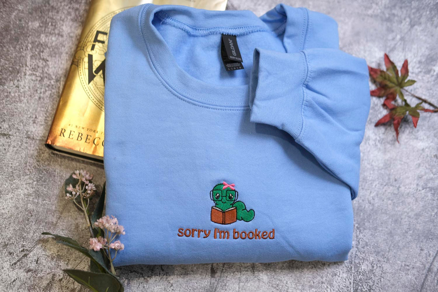 a blue sweatshirt with a cartoon character and text, along with a book and some flowers.