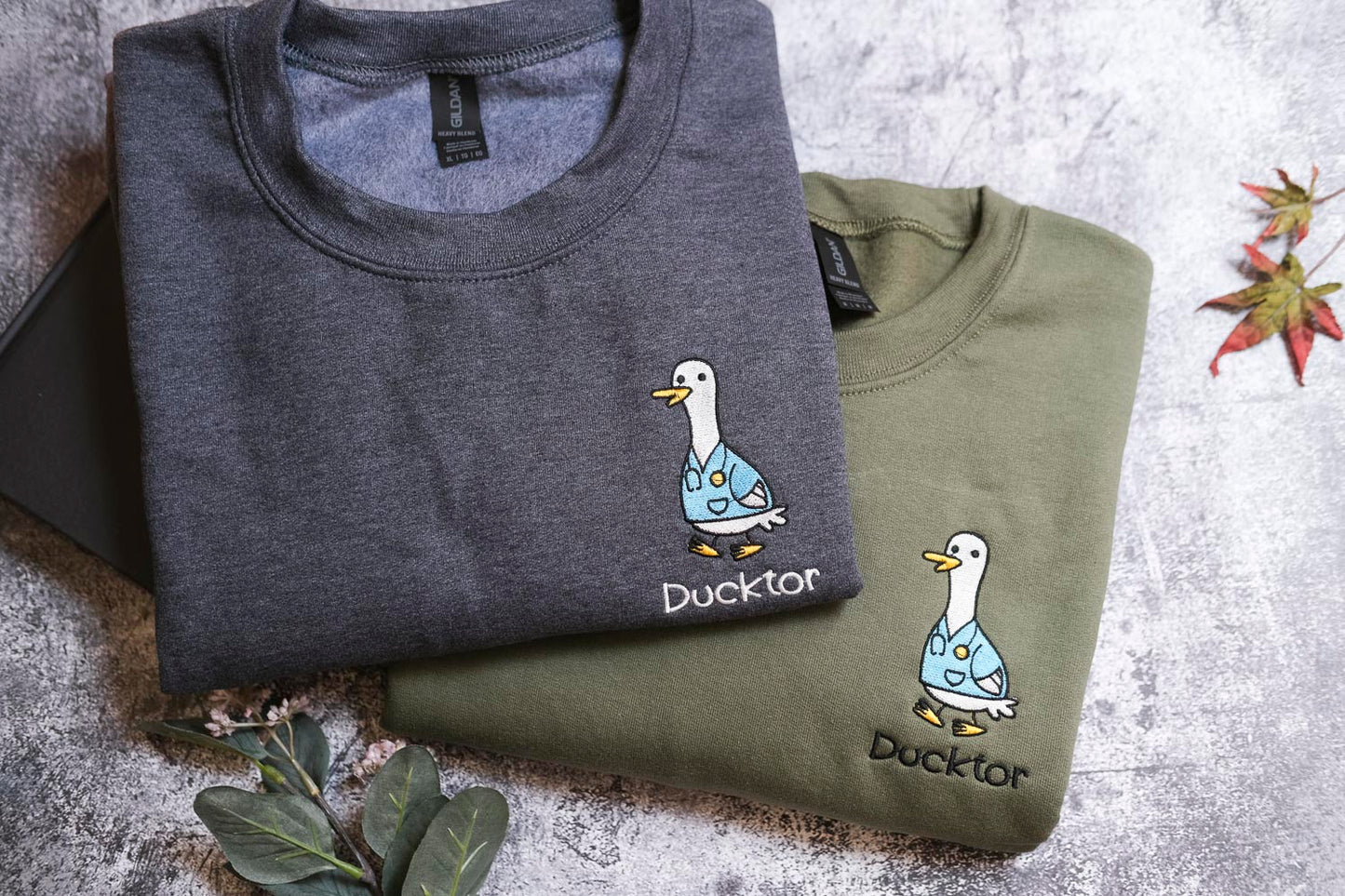 two t-shirts with a cartoon duck design, one gray and one green, both with the word "Duckster" printed on them.
