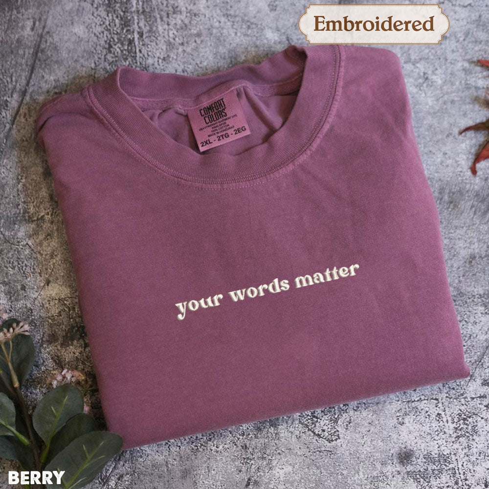 A purple t-shirt with the text "your words matter" printed on it, along with a small embroidered label.