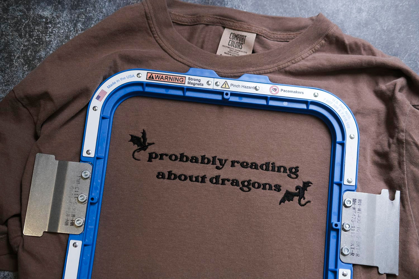A brown t-shirt with a blue frame and the text "probably reading about dragons" printed on it.