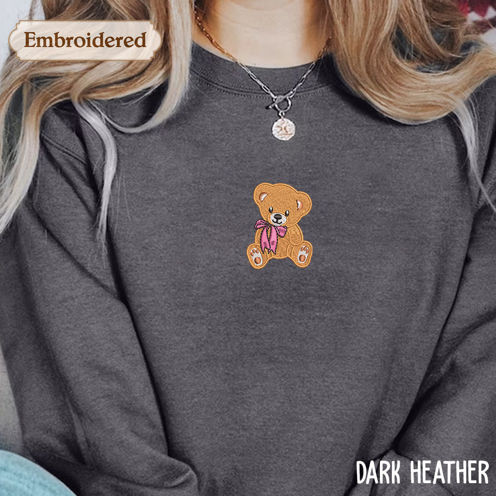 A close-up of a person wearing a gray sweatshirt with a teddy bear embroidered on the front.