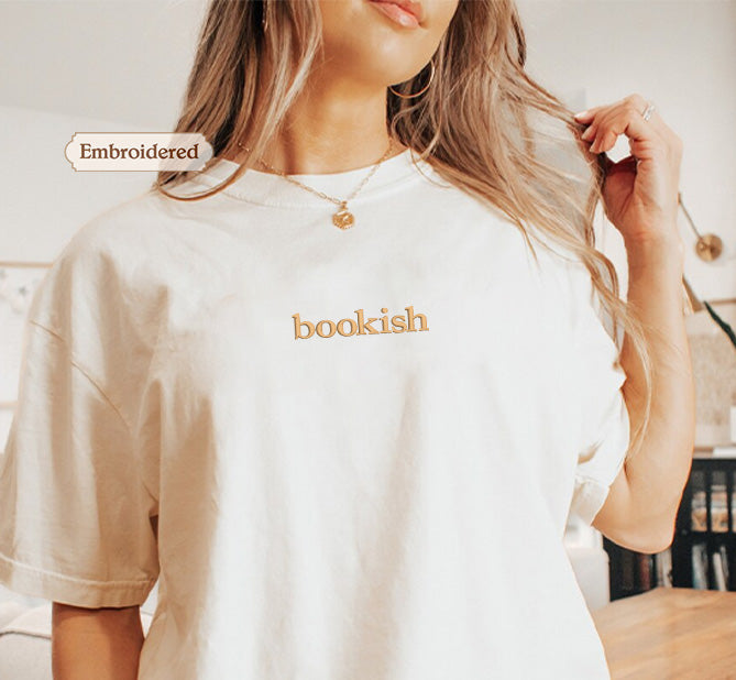 A woman wearing a white t-shirt with the word "bookish" embroidered on it, posing with her hair in her hand.