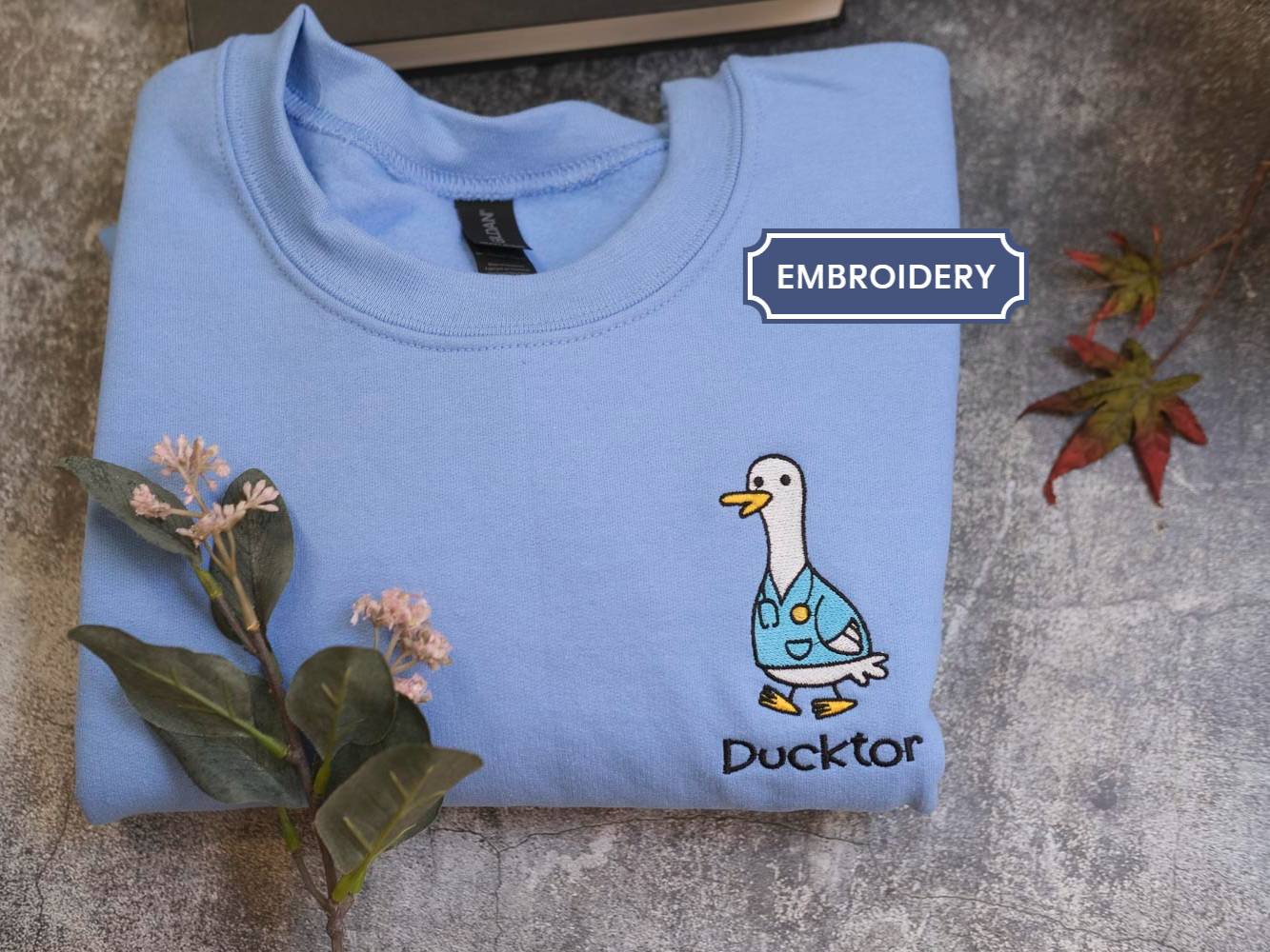 A light blue t-shirt with a cartoon duck and the word "Duckster" printed on it, along with some flowers and leaves.