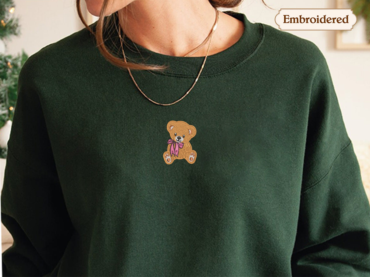 A close-up of a person wearing a green sweater with a teddy bear embroidered on it.