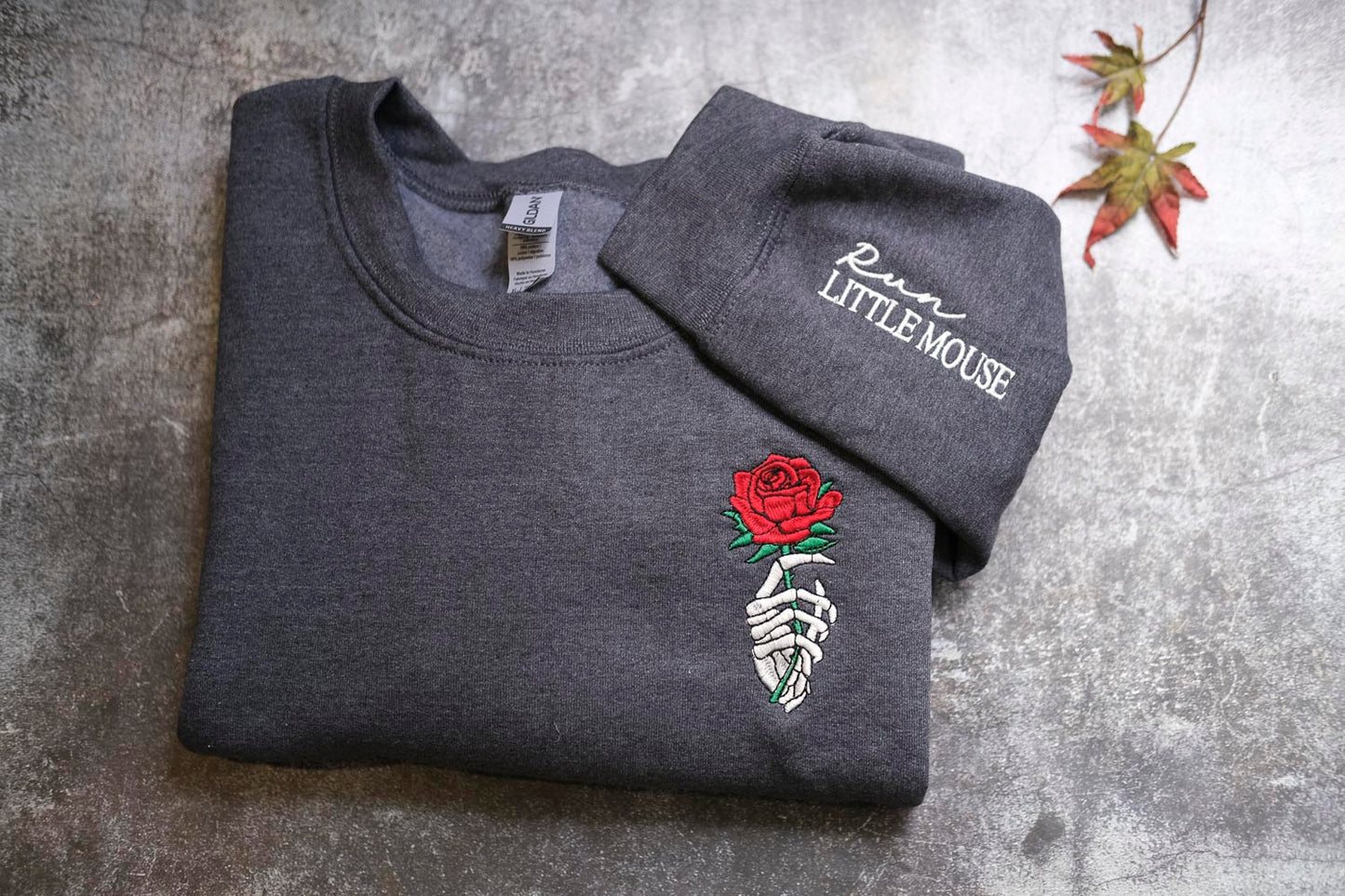 A gray sweatshirt with a red rose embroidered on the front and the text "Run LITTLE MOUSE" printed on the sleeve.