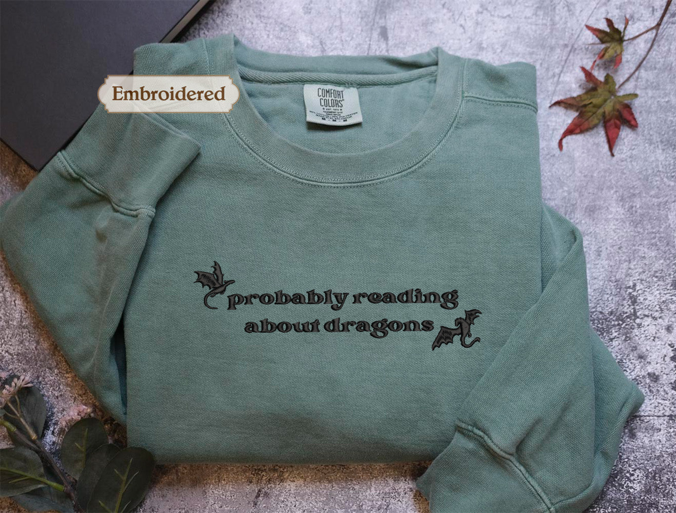 A light green long-sleeved t-shirt with the text "probably reading about dragons" printed on it, along with a small embroidered label on the collar.