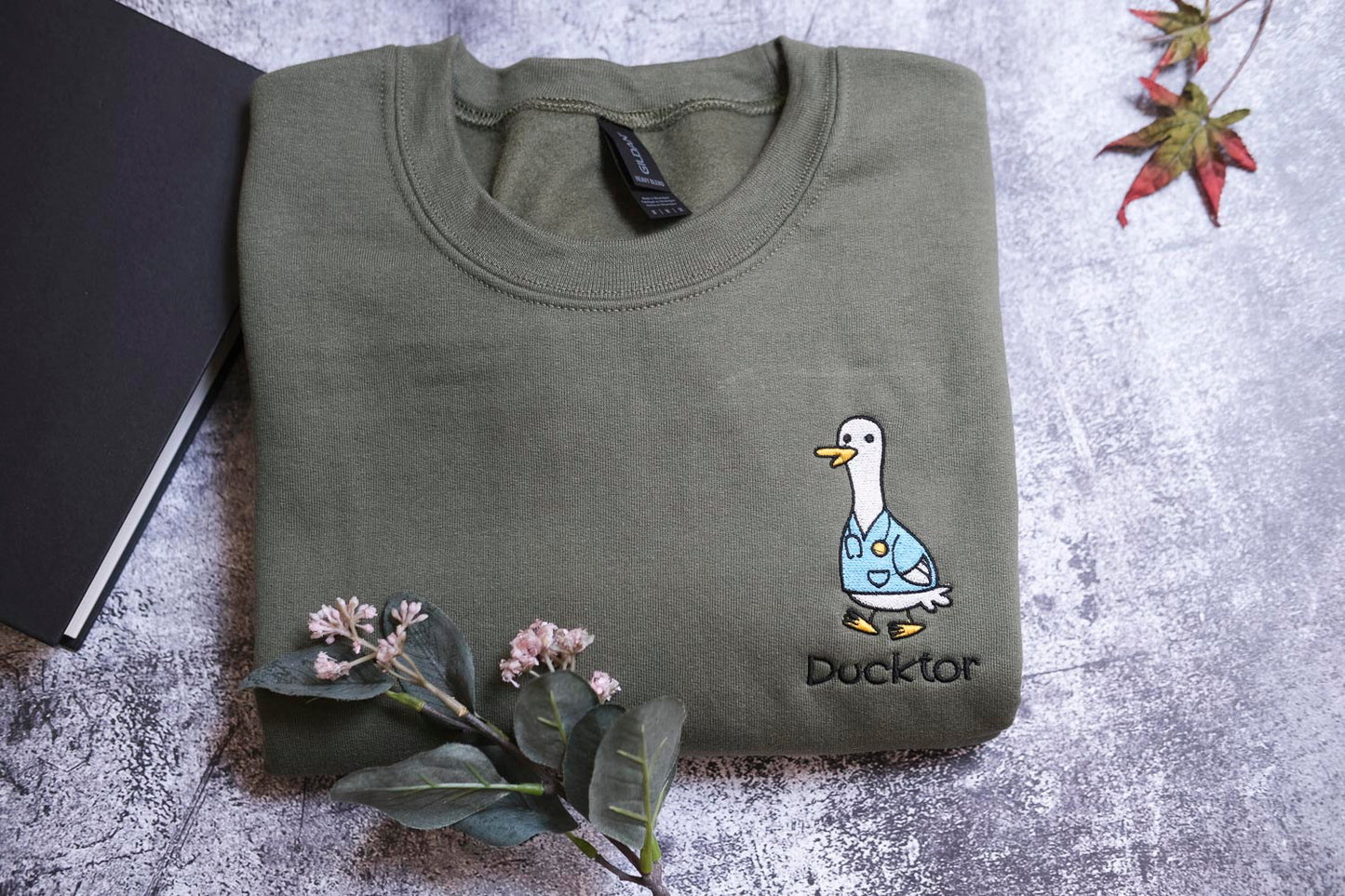 a green t-shirt with a cartoon duck and the word "Duckster" printed on it, along with a small plant and a leaf.
