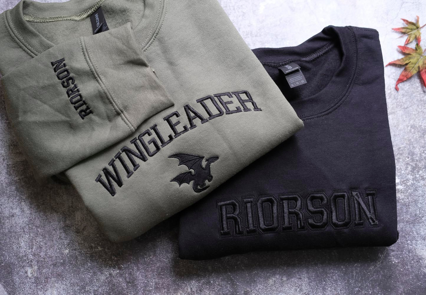 two t-shirts, one gray and one black, with the gray t-shirt featuring a dragon design and the black t-shirt with the name "Rierson" embroidered on it.