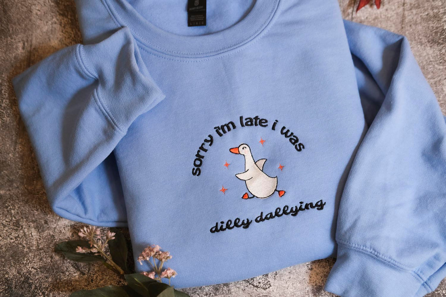 A light blue sweatshirt with a humorous text and graphic design printed on it.