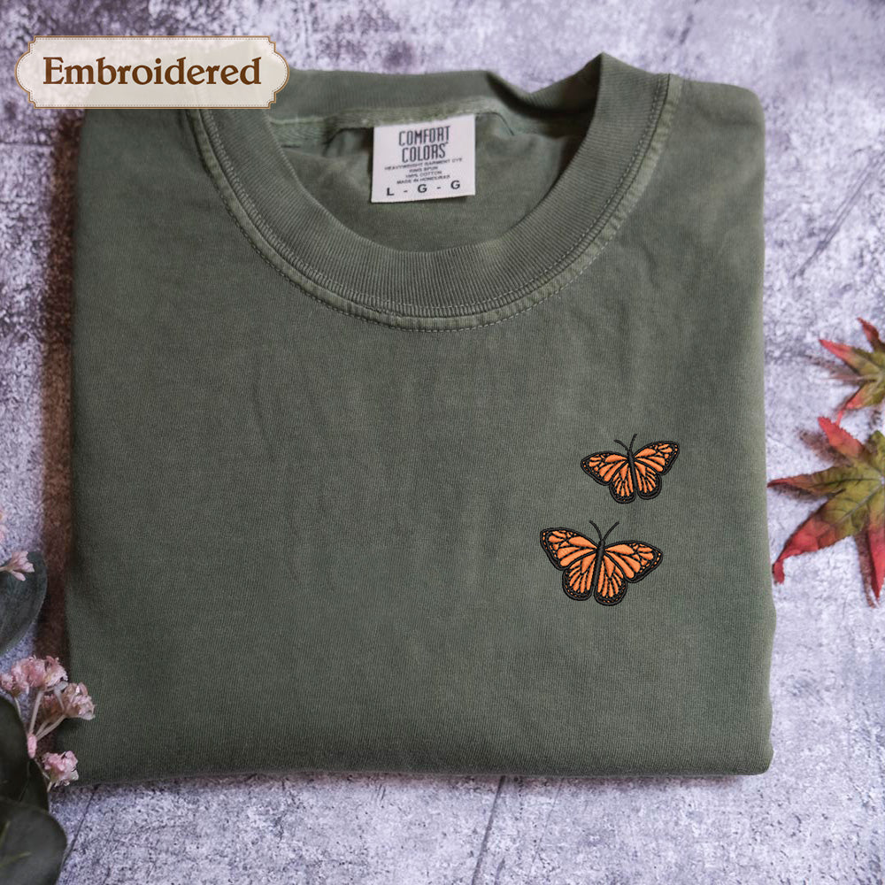 a green t-shirt with a small embroidered design of two orange butterflies on the front.