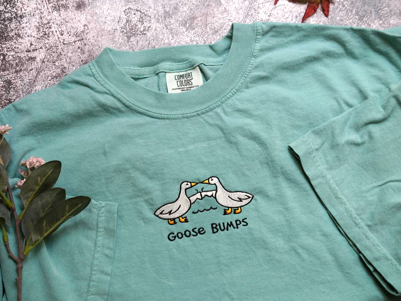 A light green t-shirt with a graphic design of two ducks and the text "Goose Bumps" printed on it.