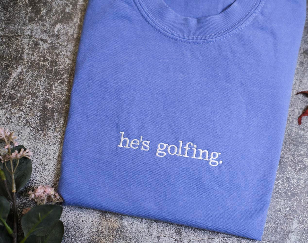 a blue t - shirt with the words he's golfing printed on it