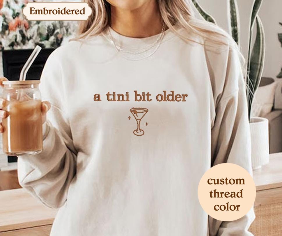 a woman is holding a drink and wearing a sweatshirt