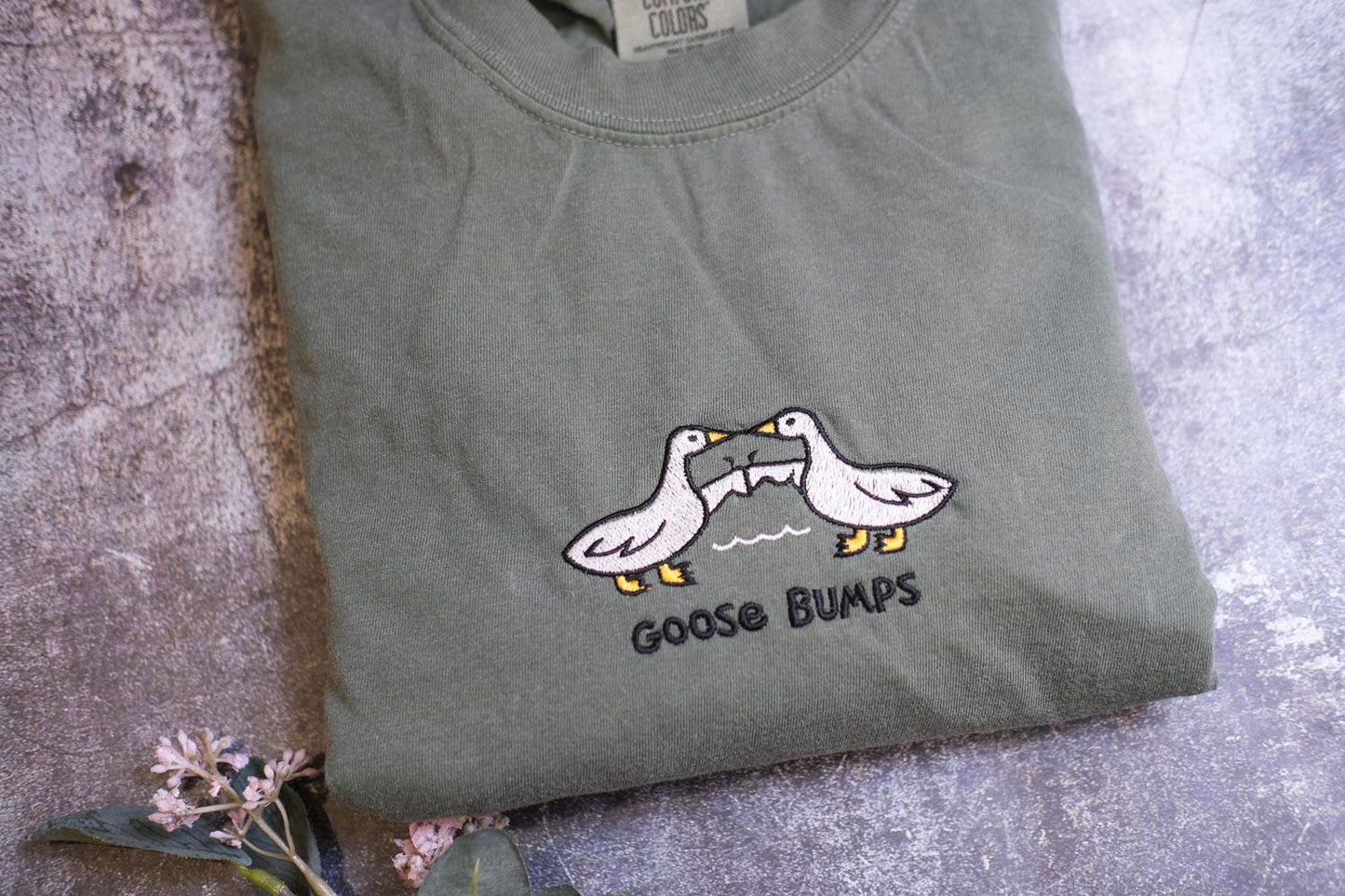a pair of geese on a t - shirt next to a flower