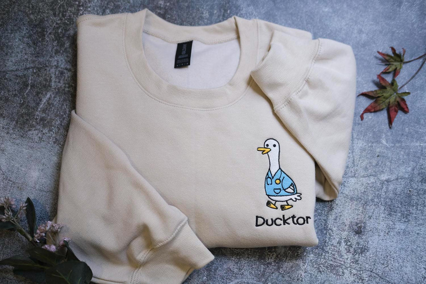 a sweater with a duck on it sitting next to a flower