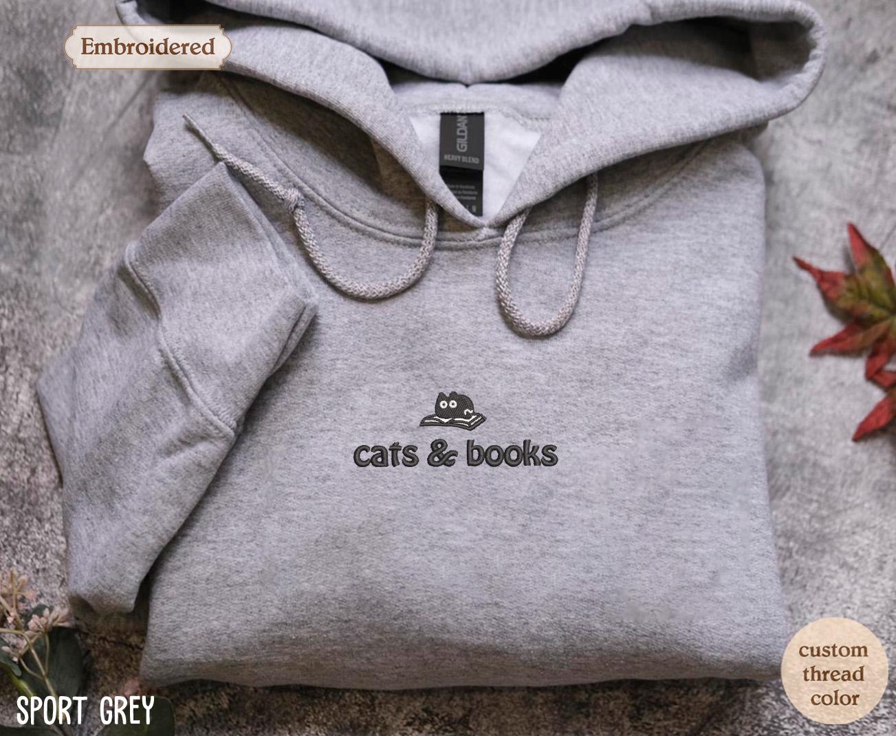 a grey sweatshirt with a cat and books on it