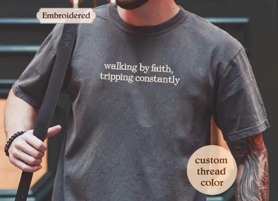a man wearing a t - shirt that says walking by faith, tripping constantly