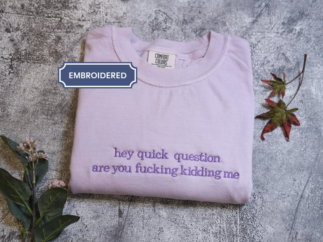 a purple t-shirt with the text "hey quick question are you fucking Kiddin Me" printed on it, along with some leaves and flowers.
