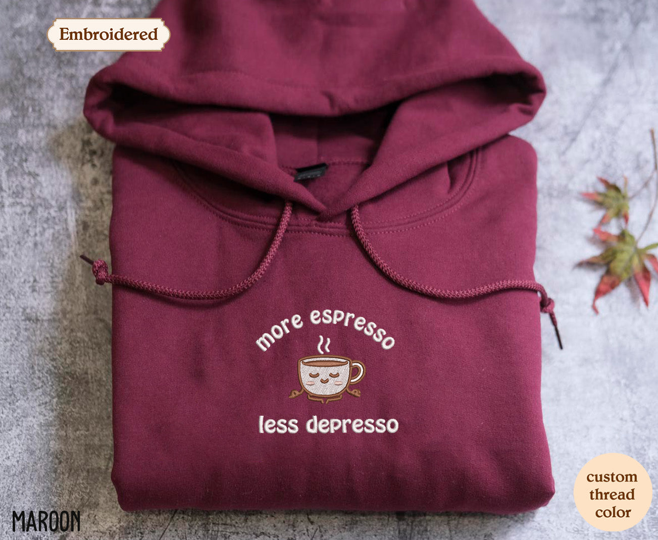 A burgundy hoodie with a white embroidered design on the front, featuring a coffee cup and the text "more espresso less depression".