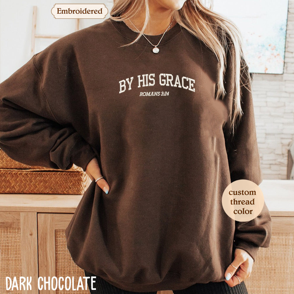 A woman wearing a brown sweatshirt with the text "BY HIS GRACE ROMANS 3:24" printed on it.