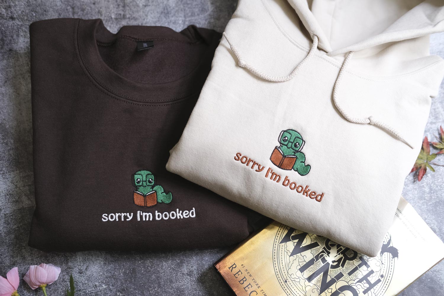 two t-shirts with a humorous text and a small green character on them, along with a book titled "The Wings of the Wisp".