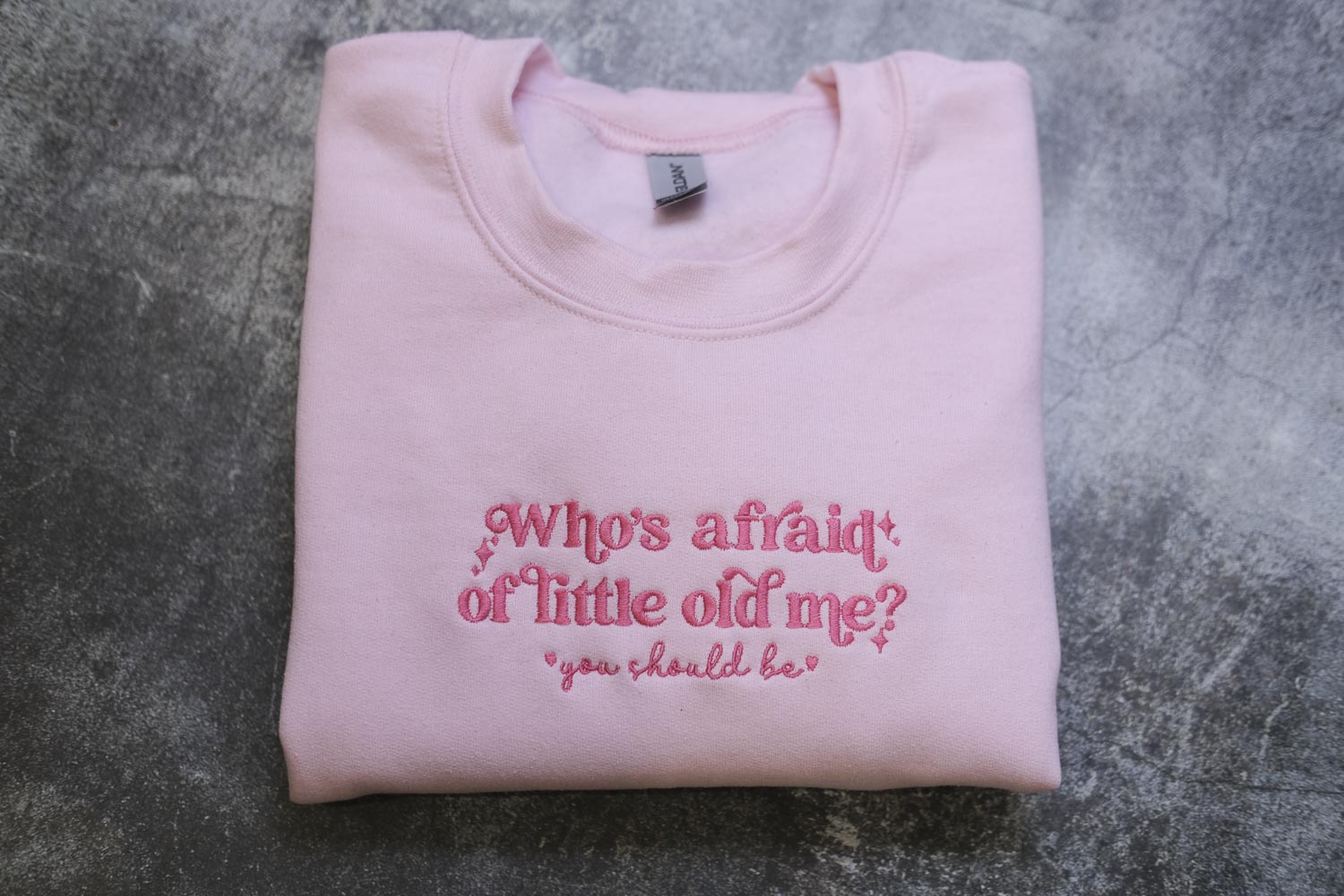 A pink sweatshirt with the text "Who's afraid of little old me? you should be" embroidered on it.