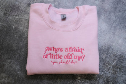 A pink sweatshirt with the text "Who's afraid of little old me? you should be" embroidered on it.