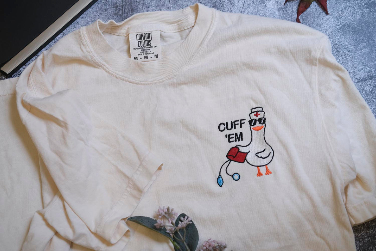 A white t-shirt with a cartoon duck wearing a nurse's hat and the text "CUFF 'EM" printed on it.