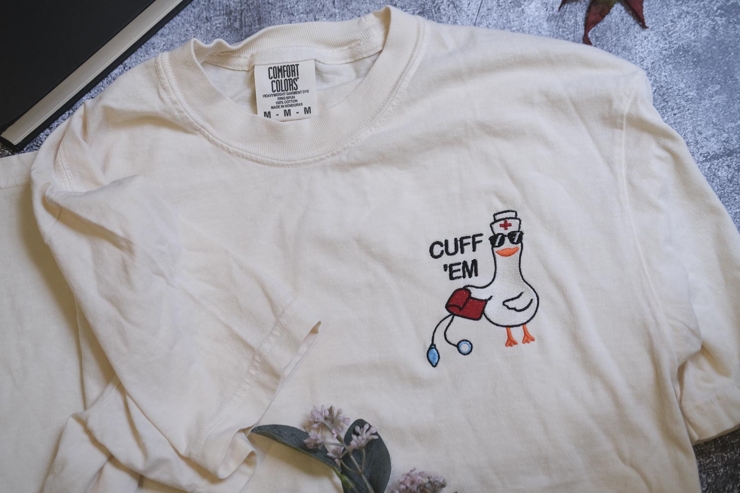 A white t-shirt with a cartoon duck wearing a nurse's hat and the text "CUFF 'EM" printed on it.