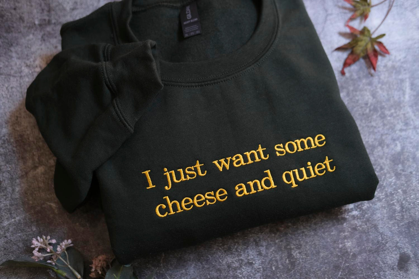 A black sweatshirt with yellow text that says "I just want some cheese and quiet" is displayed on a gray surface.